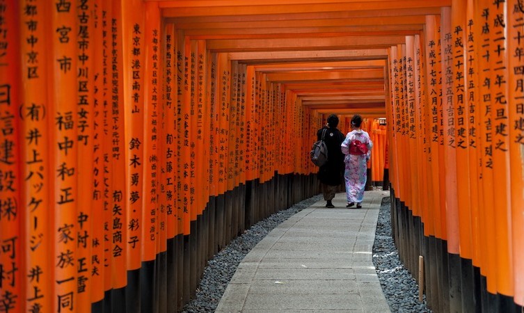 Two women walking through the gate and pathway to the Fushimi Inari Taisha Shinto Shrine.