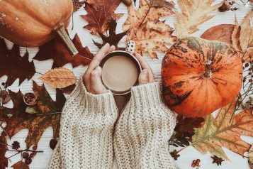 Hand,Holding,Warm,Coffee,And,Pumpkins,And,Colorful,Leaves,Top