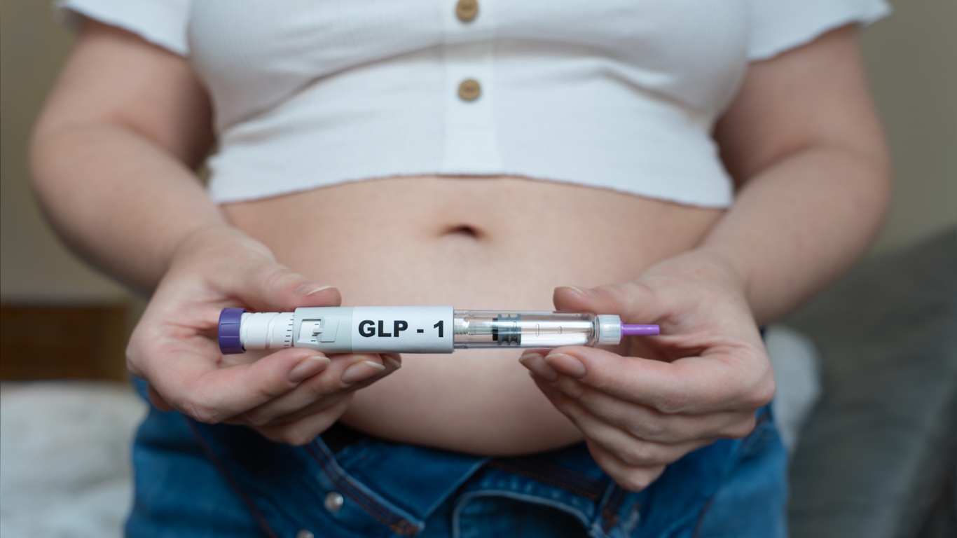woman-holding-a-GLP-1-injection-pen-in-both-hands-with-her-bare-abdomen-visible-in-the-background