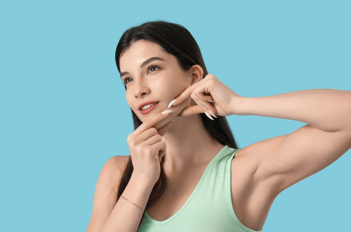 beautiful young woman doing face building exercise on blue background - Jawline contouring