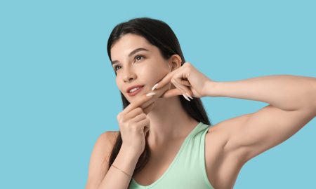 beautiful young woman doing face building exercise on blue background - Jawline contouring