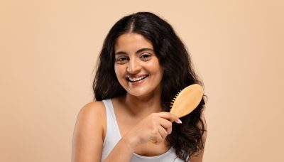 smiling beautiful indian woman brushing her thick curly hair with bamboo comb