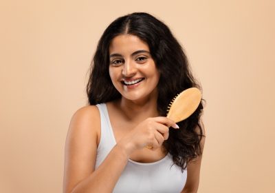 smiling beautiful indian woman brushing her thick curly hair with bamboo comb