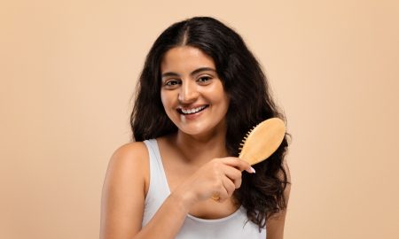 smiling beautiful indian woman brushing her thick curly hair with bamboo comb