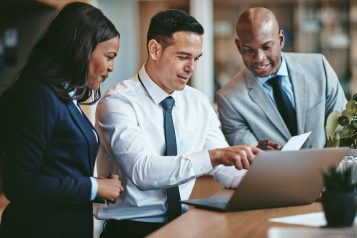 Diverse,Group,Of,Smiling,Businesspeople,Reading,Paperwork,Together,While,Working