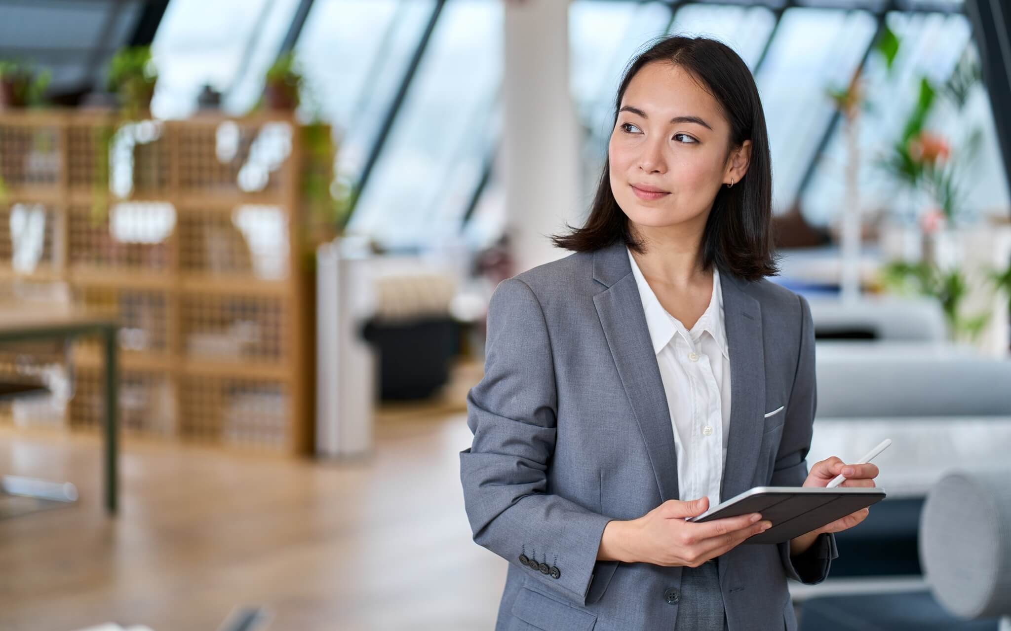 Young Asian business woman entrepreneur standing in office holding digital tablet