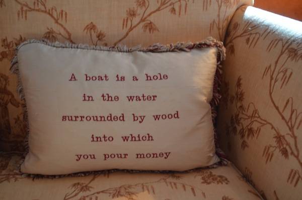 A pillow on a yacht saying “A boat is a hole in the water surrounded by wood into which you pour money”