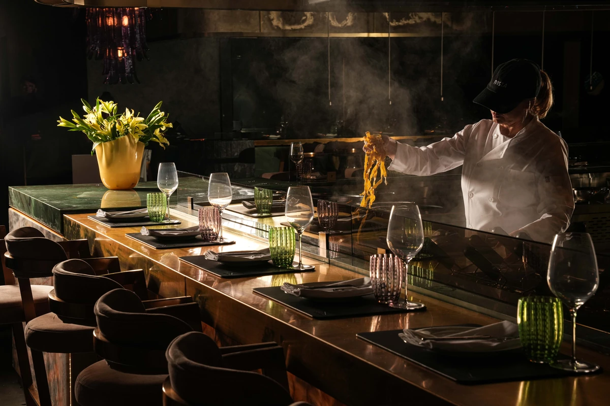 A chef lifts fresh pasta in the open kitchen behind the chef