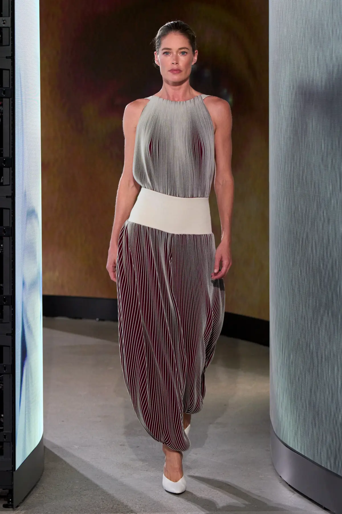 Doutzen Kroes on the Alaïa Winter Spring 2027 runway in a vertically pleated silver and burgundy top and trousers with cream waistband and white pumps