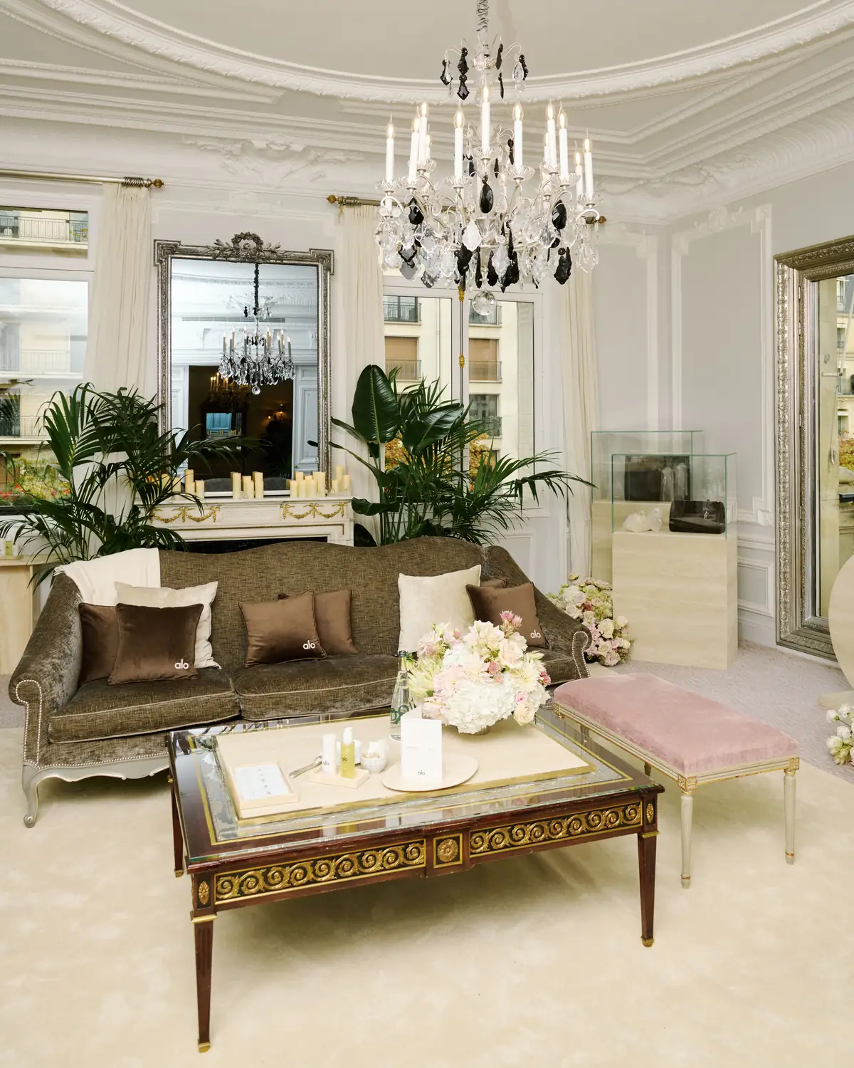 A crystal chandelier, velvet sofa with ALO cushions, and pink bench in a Parisian salon styled as the ALO Oasis for the ALO Plaza Athénée takeover