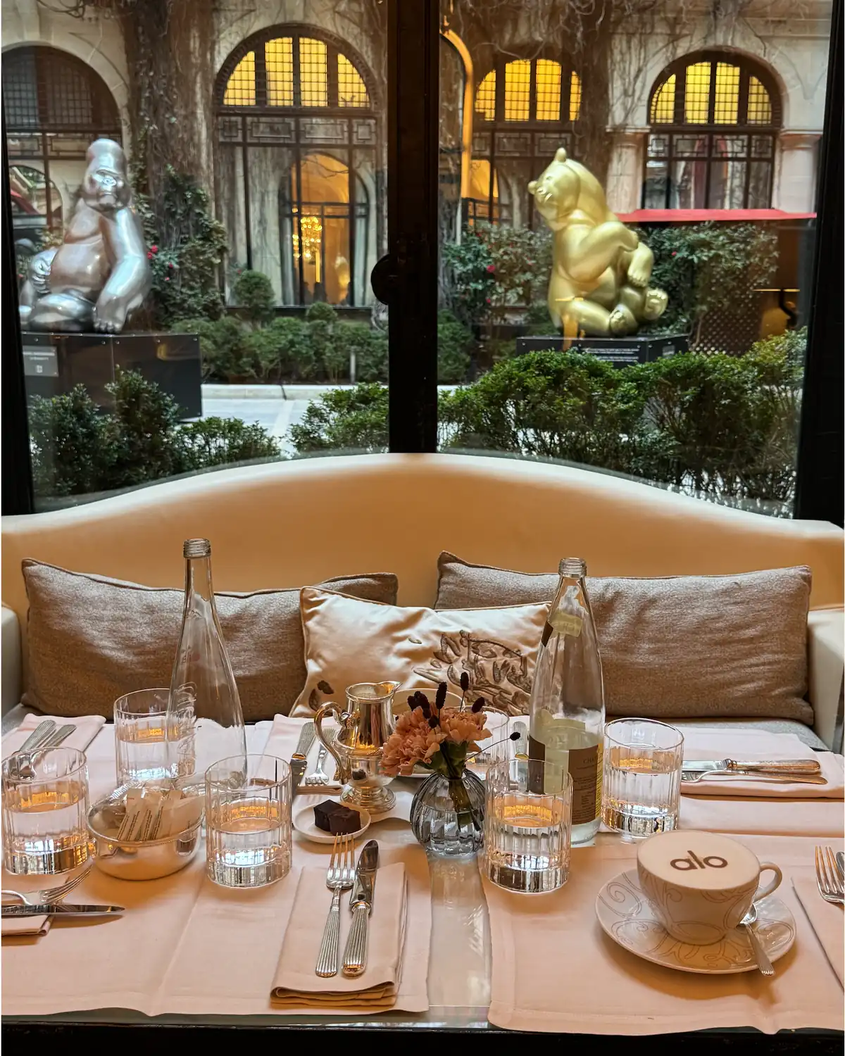 A breakfast table set with an ALO-branded cup beside a window overlooking the courtyard sculptures, part of the ALO Plaza Athénée Paris Fashion Week menu takeover