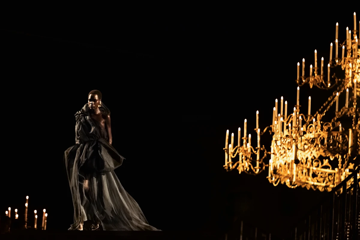 A model in a black evening gown walks past a candlelit chandelier at Anthony Vaccarello