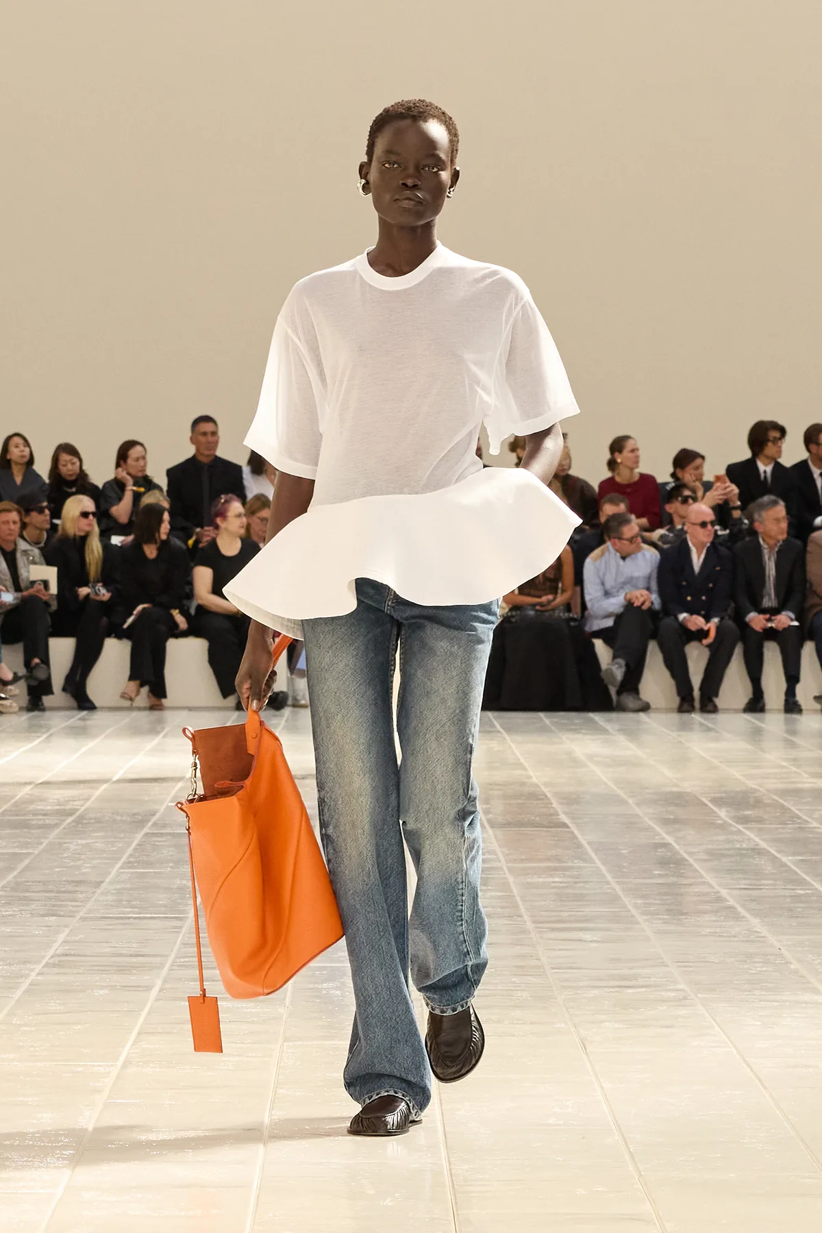 Model in a white t-shirt with a flared peplum hem, light blue jeans and an orange bag in Balenciaga Summer 2027 Look 35