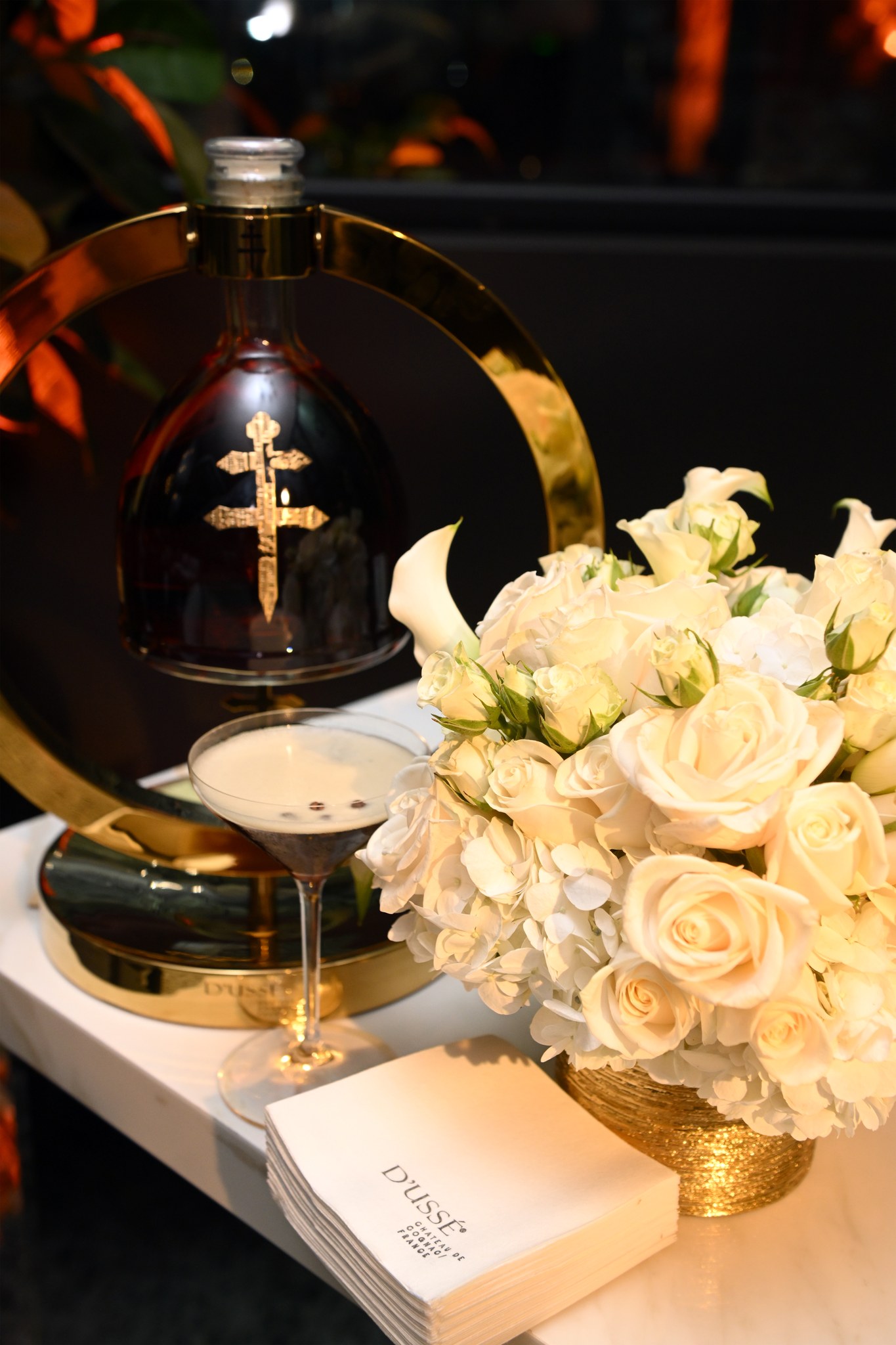 A D’USSÉ cocktail served beside a bottle display and white roses at Gravitas