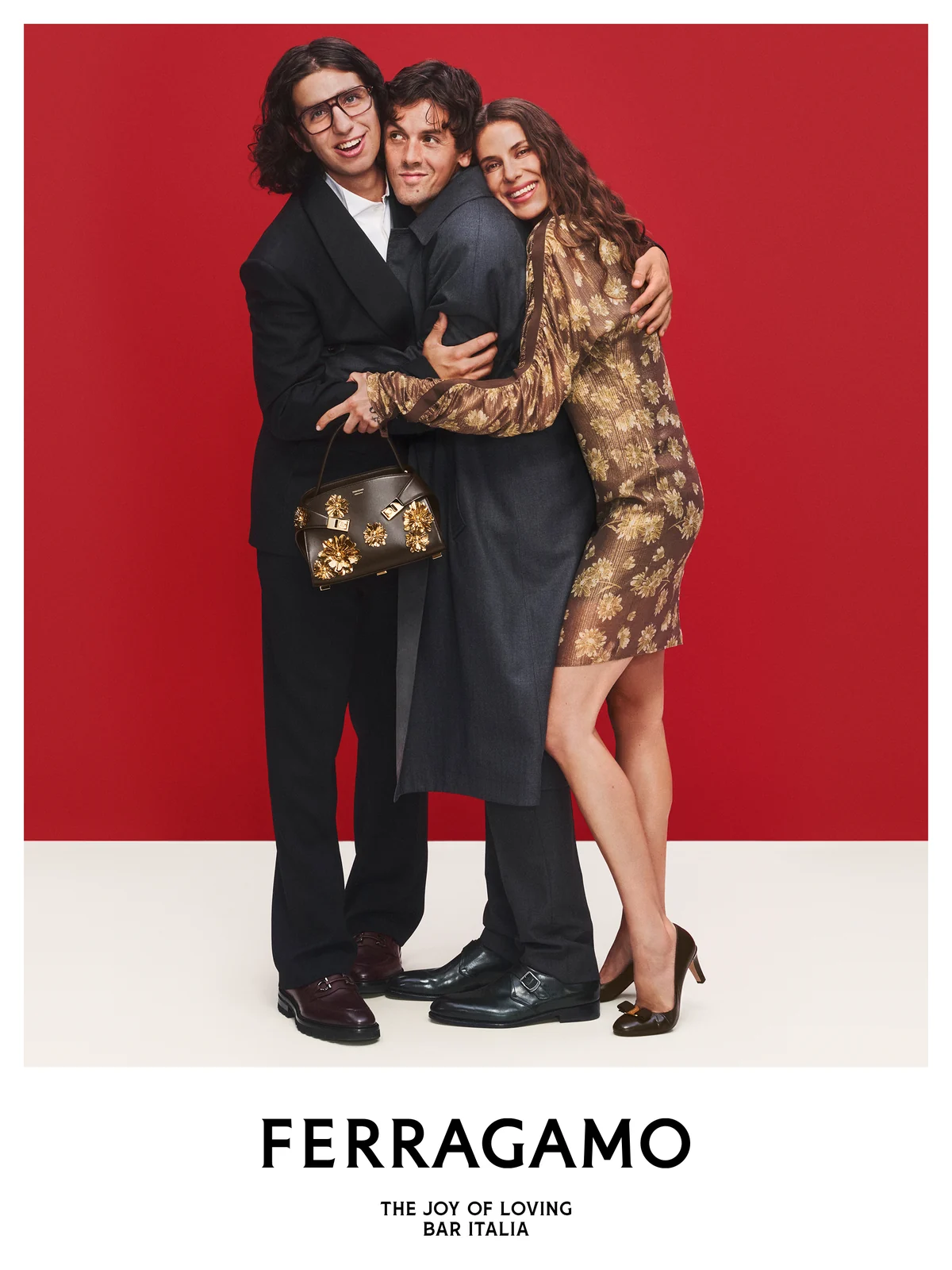 The three members of Bar Italia embracing in the Ferragamo holiday campaign, one holding a gold-embellished Ferragamo bag