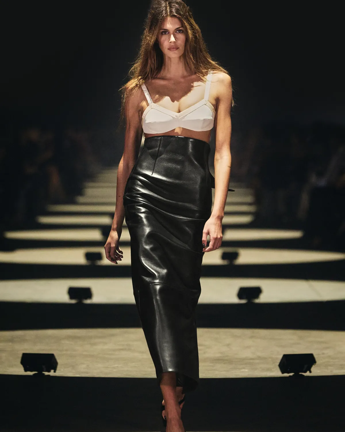 Khaite Spring 2027 Look 1, Kaia Gerber in a white bra top and leather skirt, at New York Fashion Week