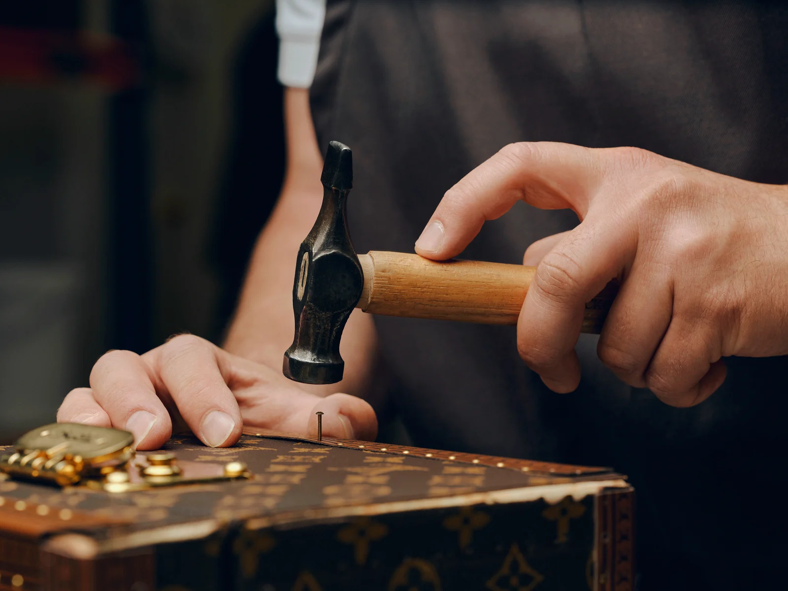 Louis Vuitton Care & Repair: artisan hammering brass hardware on a Monogram trunk