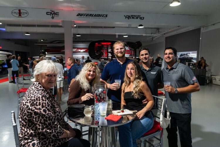 Guests at a cocktail table during the Outerlimits Powerboats reception at the new Fort Lauderdale dealership, with Outerlimits and CMC Boat Group banners behind them