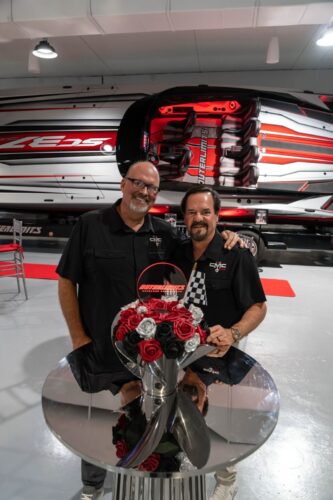 Two hosts in Outerlimits shirts standing beside the red Outerlimits SC37 catamaran at the Fort Lauderdale dealership