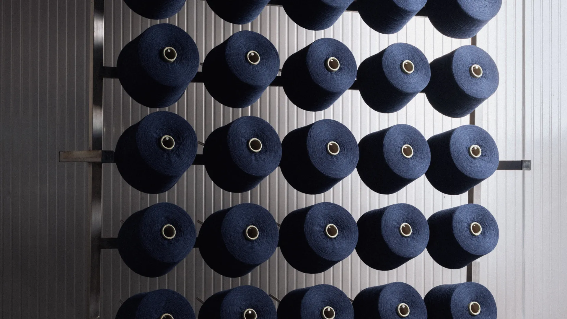 Navy Prada Re-Cashmere yarn cones lined up on a spinning rack in Italy