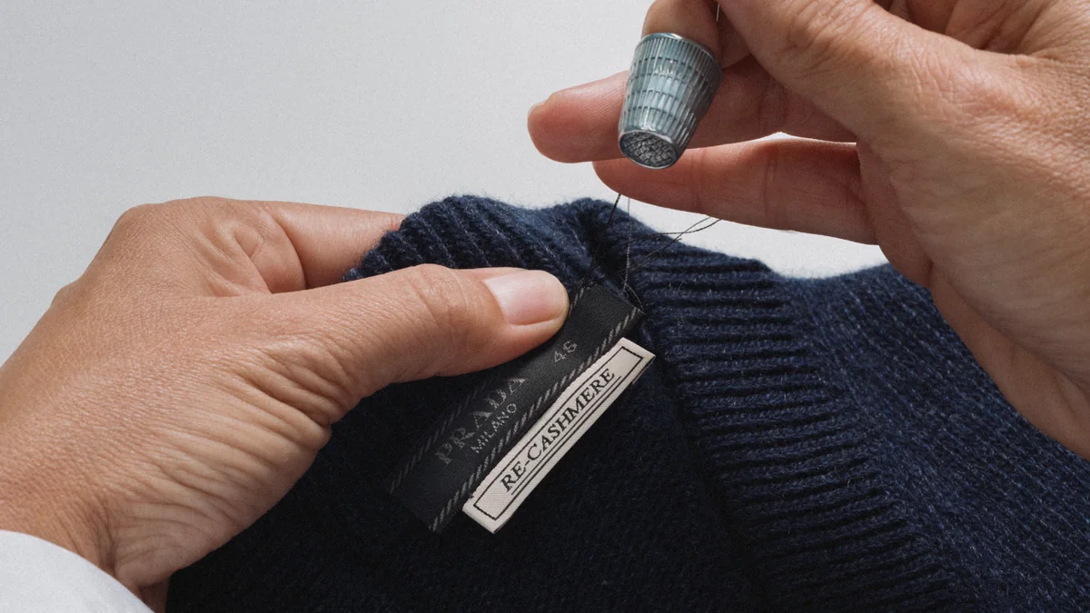 Artisan hand-sewing the label into a navy Prada Re-Cashmere sweater