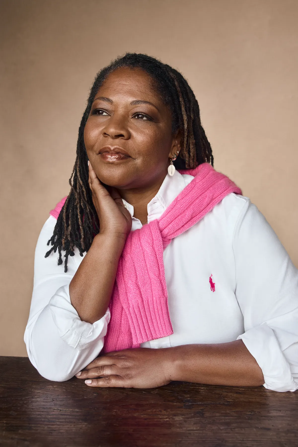 Dr. Chanita Hughes-Halbert in a white shirt with a pink sweater over her shoulders, seated at a wooden table, in the Ralph Lauren Pink Pony 2026 campaign