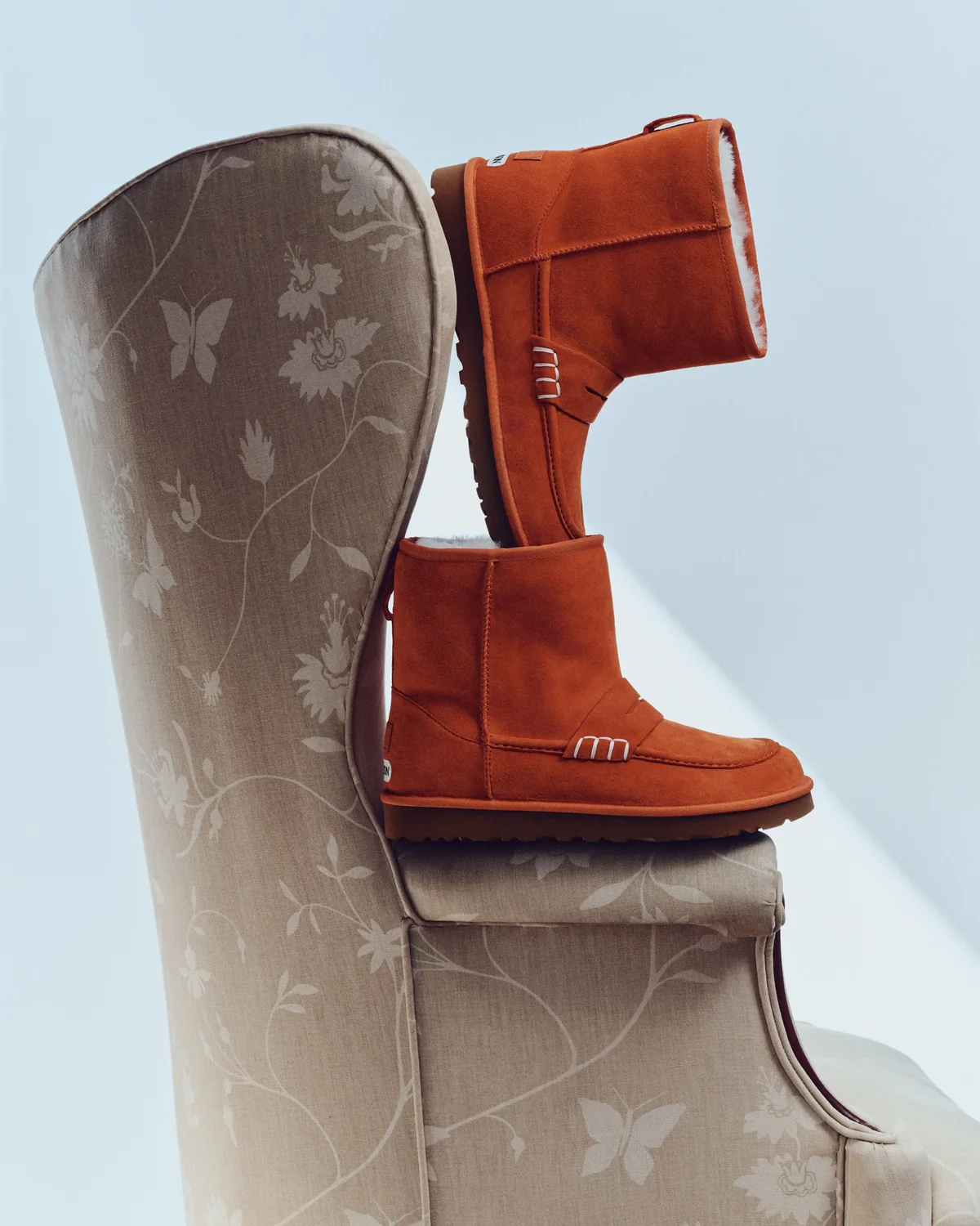 Ugg x JW Anderson loafer boots in Orange stacked on a floral armchair