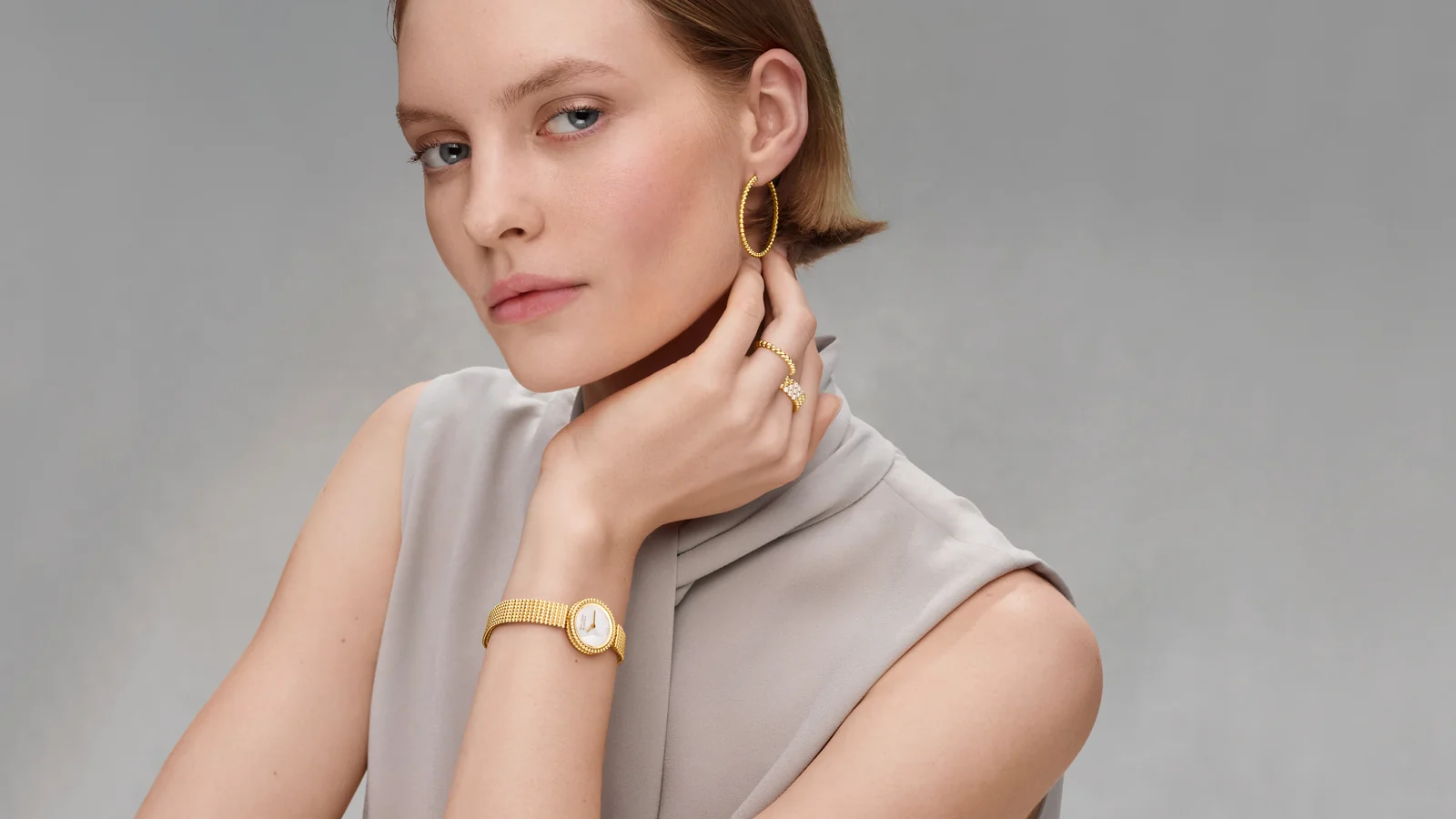 Model wearing a Perlée gold watch, hoop earring and rings, Van Cleef Perlée Las Vegas campaign image